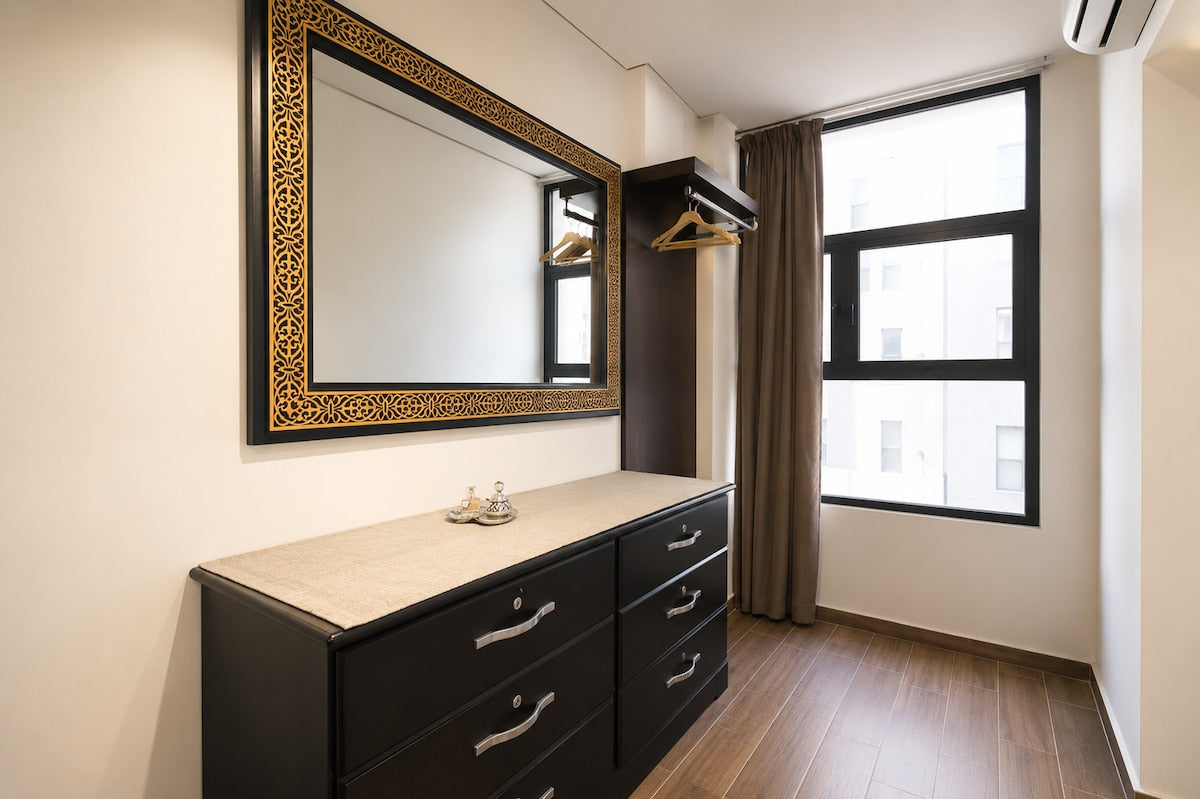 Bedroom storage area with dresser, large mirror and natural light in Haut Founty.