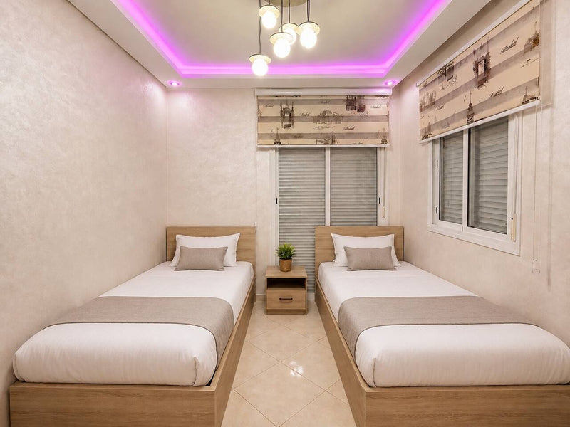 Twin bedroom with two single beds and purple ceiling lighting in Hay Mohammadi.